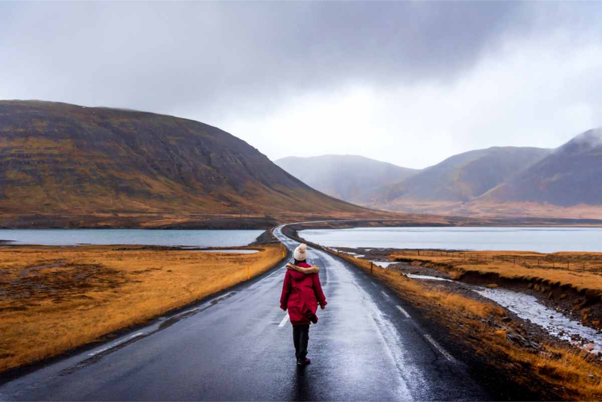 Woman standing in the middle of an empty road surrounded by golden meadows on a cloudy day