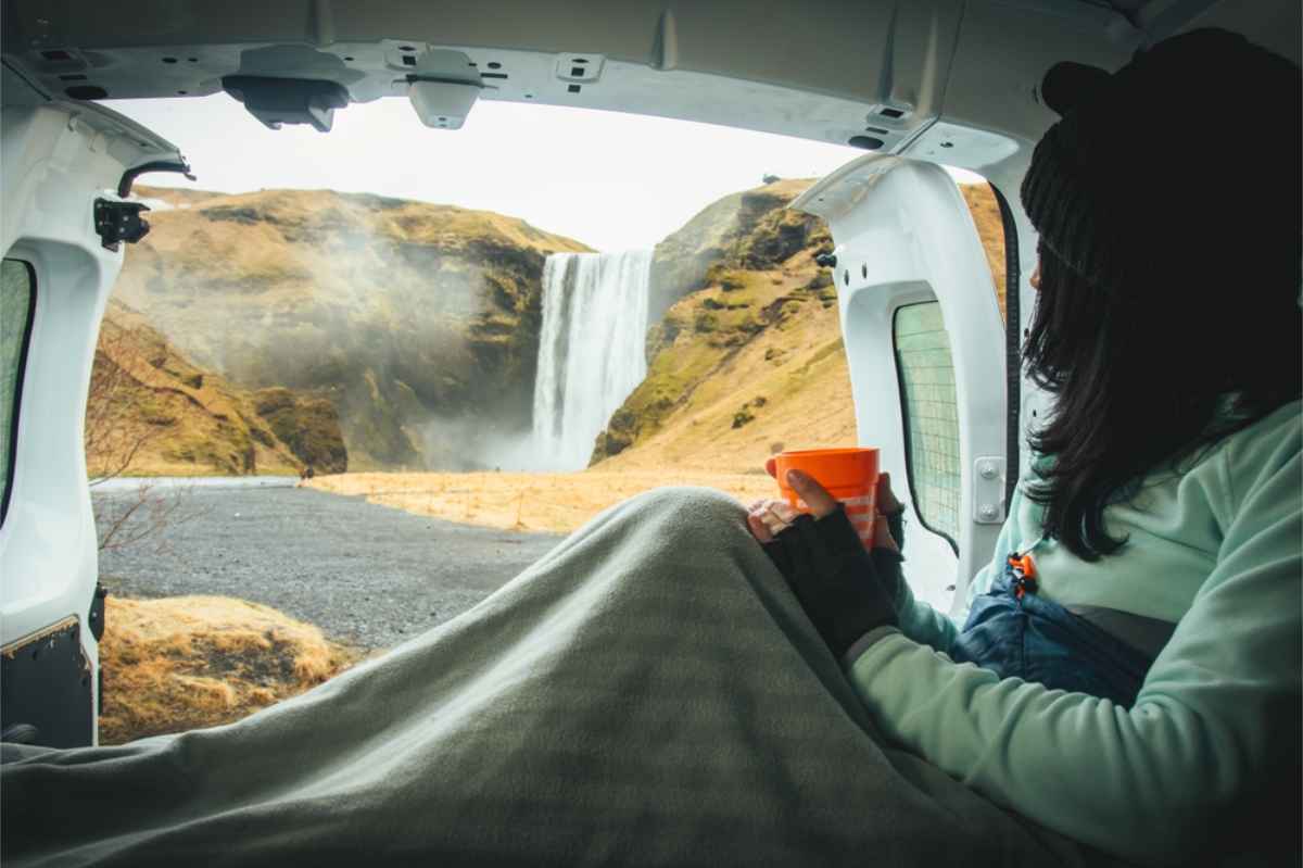 Woman resting in her campervan while looking at an impressive waterfall