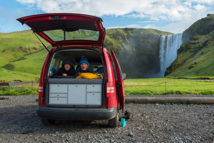 Two tourists inside of their campervan parked by a waterfall