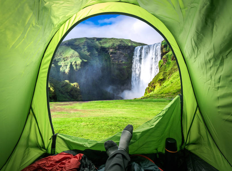 camper inside of his tent placed in front of a waterfall