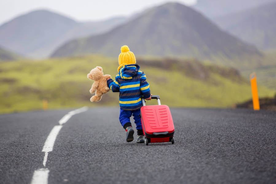 kid wheeling a carry-on bag on a road representing a road trip in Iceland with babys