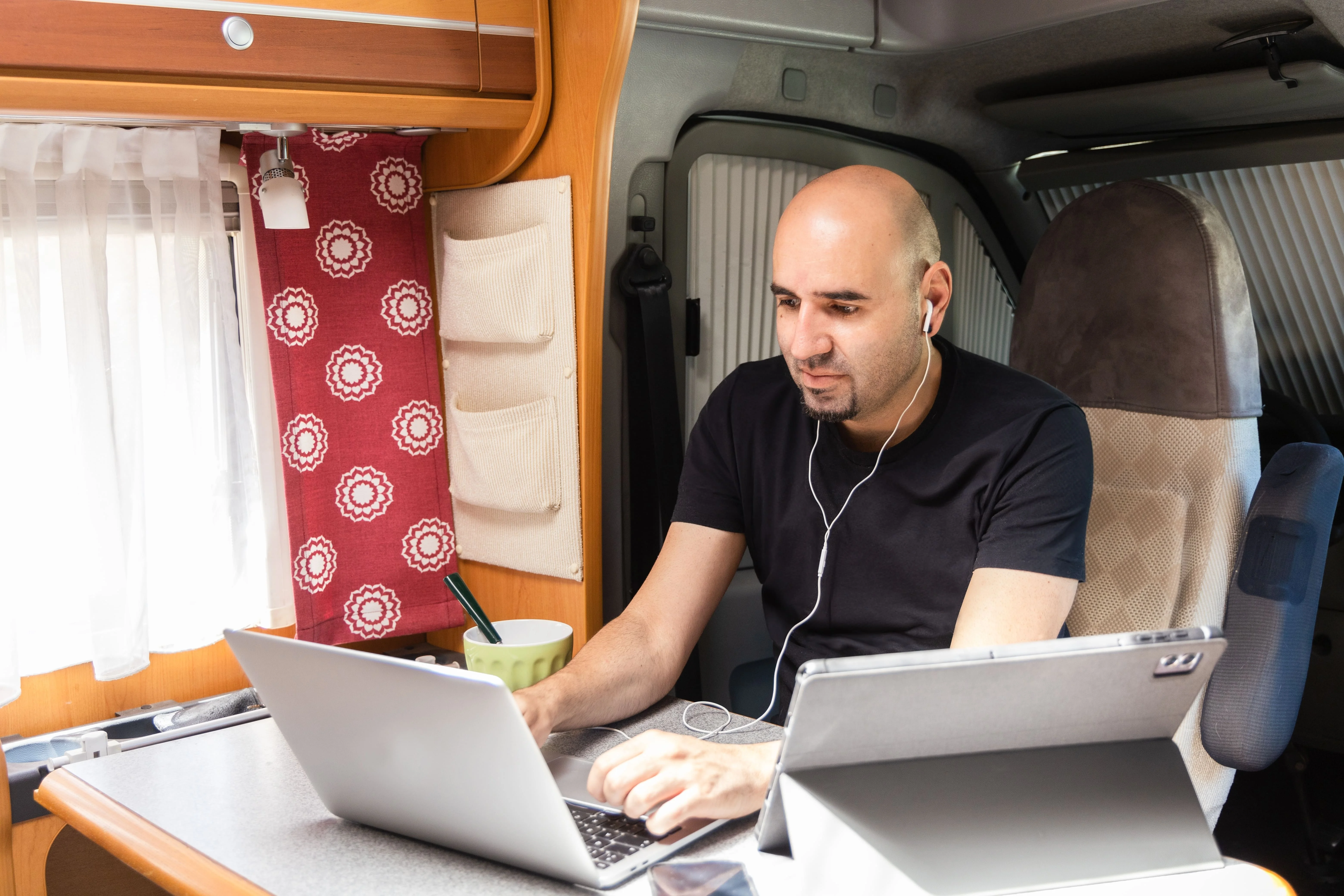 Digital Nomad Working from an RV – Vanlife Remote Work Setup Man working remotely from an RV using a laptop and tablet, showcasing a digital nomad vanlife workspace.