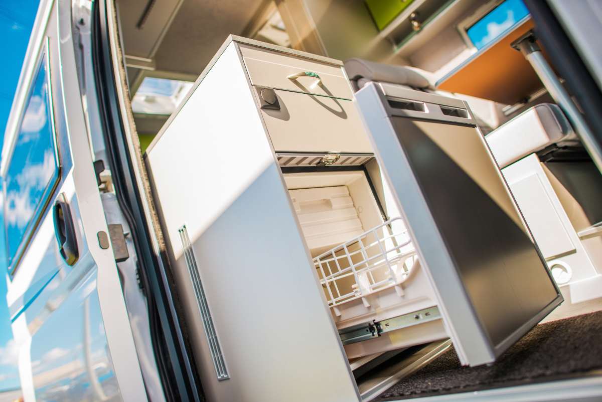 A close-up of an open pull-out refrigerator in a modern RV kitchen. The sleek design showcases compact and efficient storage, emphasizing the importance of securing items inside to prevent spills and breakage while driving.