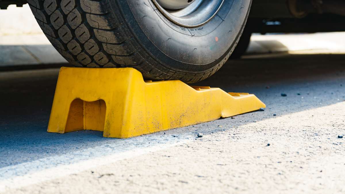 A close-up of an RV tire resting on a yellow leveling block, placed on asphalt to stabilize the vehicle. The leveling kit helps ensure a balanced and secure setup, especially on uneven terrain or inclined surfaces, preventing unwanted movement.