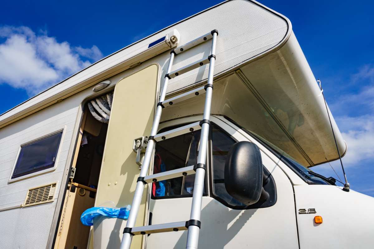 A telescopic extension ladder leaning against an RV, providing access to the over-cab sleeping area. The lightweight aluminum design makes it ideal for maintenance and repairs, ensuring easy storage and portability for RV owners.