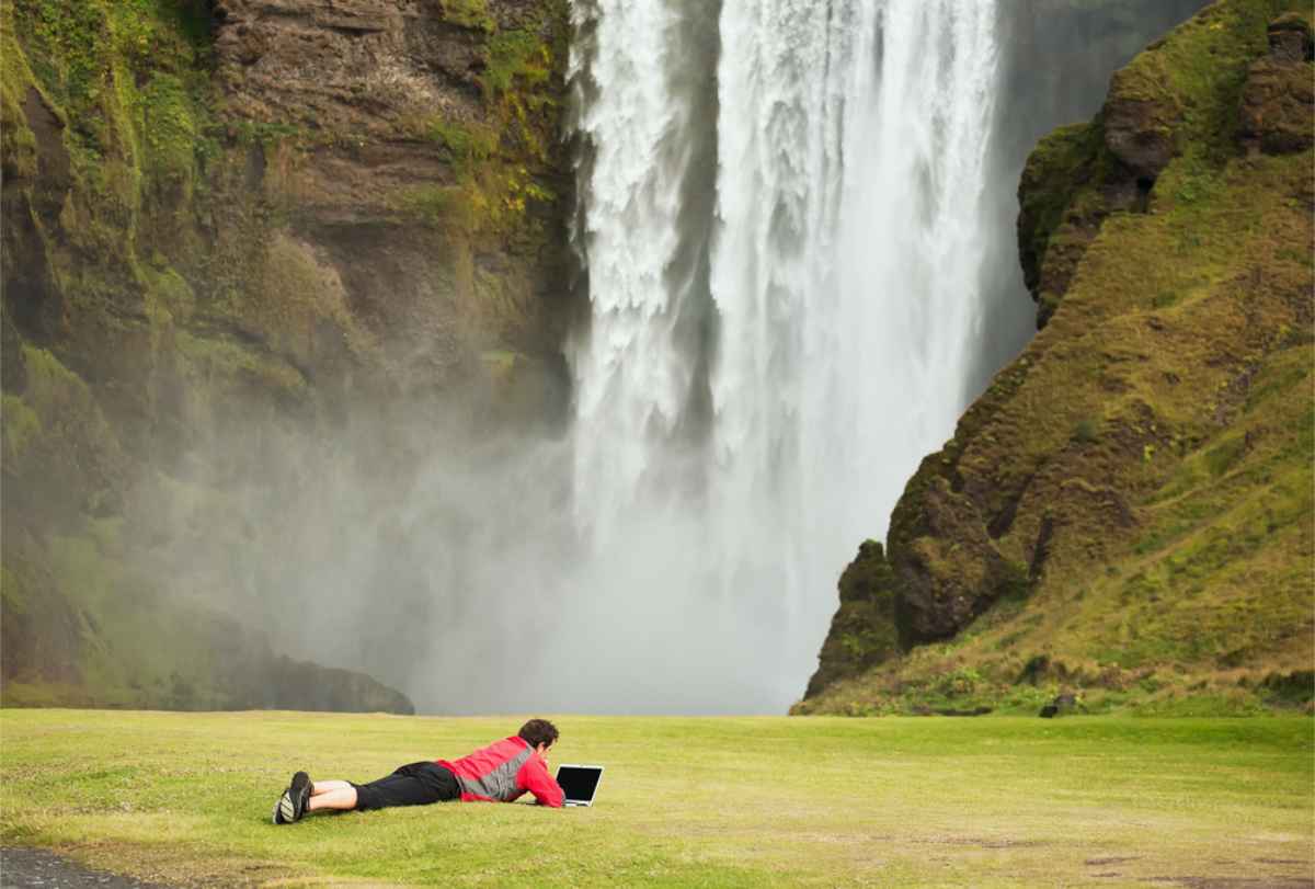 man working remotely in Iceland laying on the grass close to Skogafoss waterfall