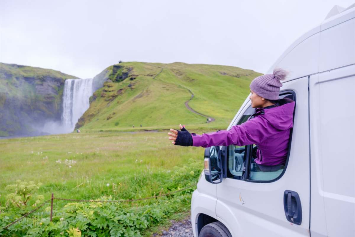 Camper driver sticking her hand out of her camper window while watching Skogafoss waterfall