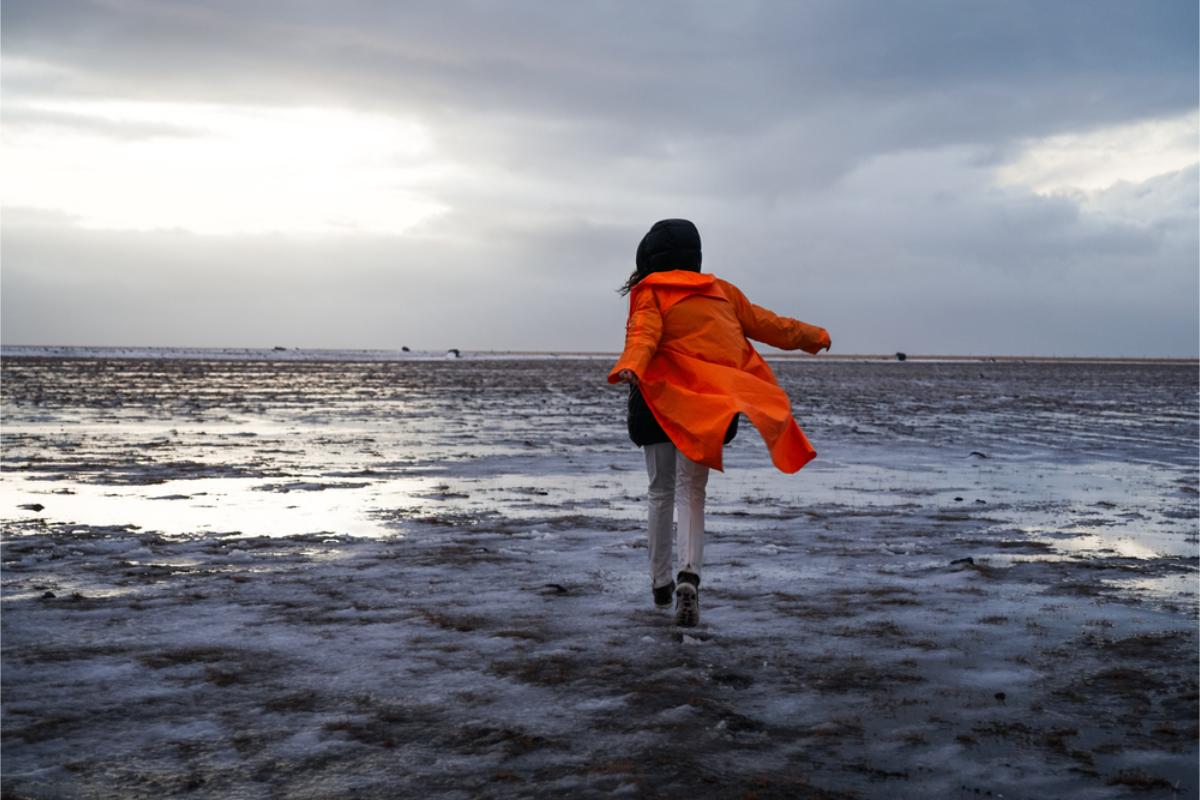 Tourist in a orange jacket walking on icy road and through hard winds