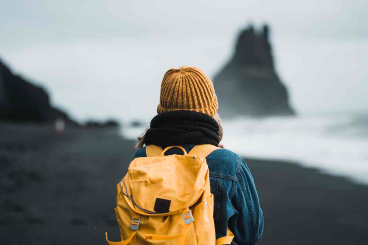woman with a yellow backpack and beanie at Reynisfjara beach in Iceland