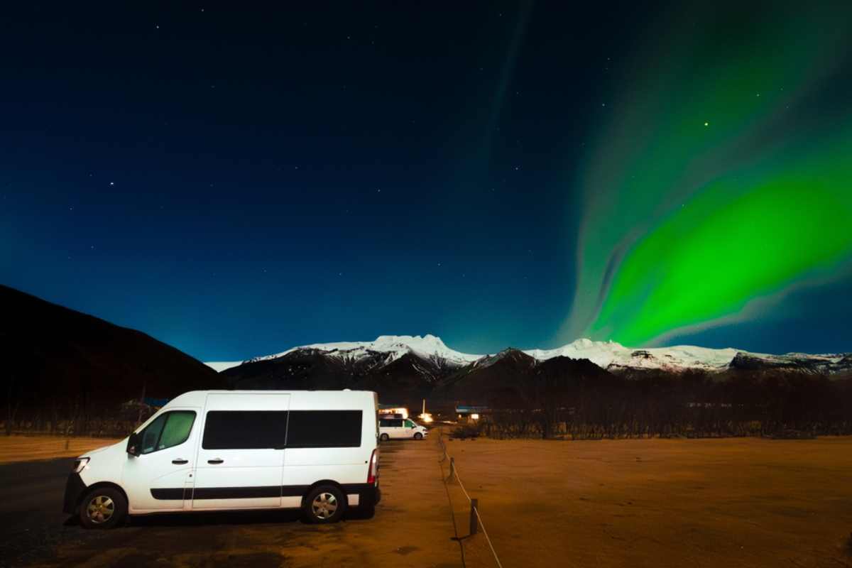 White campervan parked in a designated area with a green northern light dancing in the sky