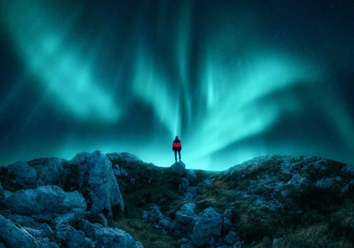 Tourit standing on top of a hill enjooying the beautiful green northern lights