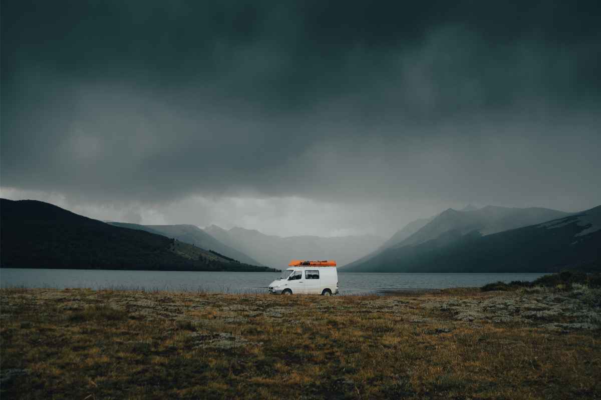White campervan parked by a lake on a dark and misty evening