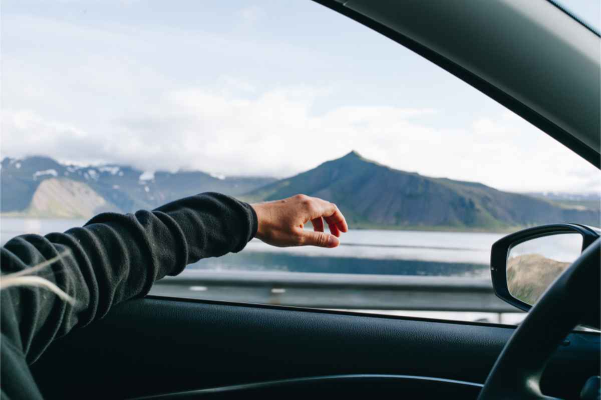 Driver sticking his arm out of the car's window with a pretty landscape at the distance