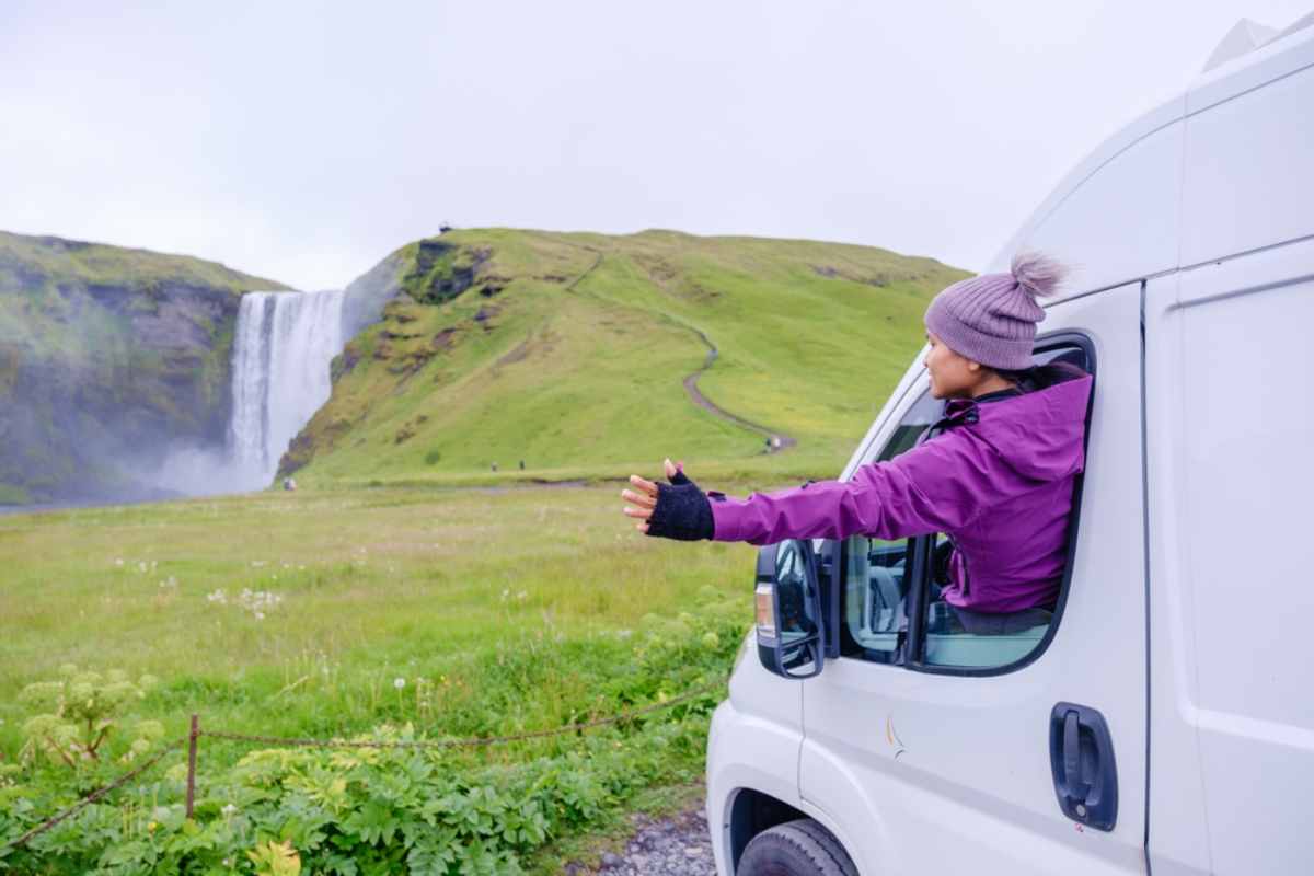 Traveler enjoying the view of Skógafoss waterfall from a campervan window.