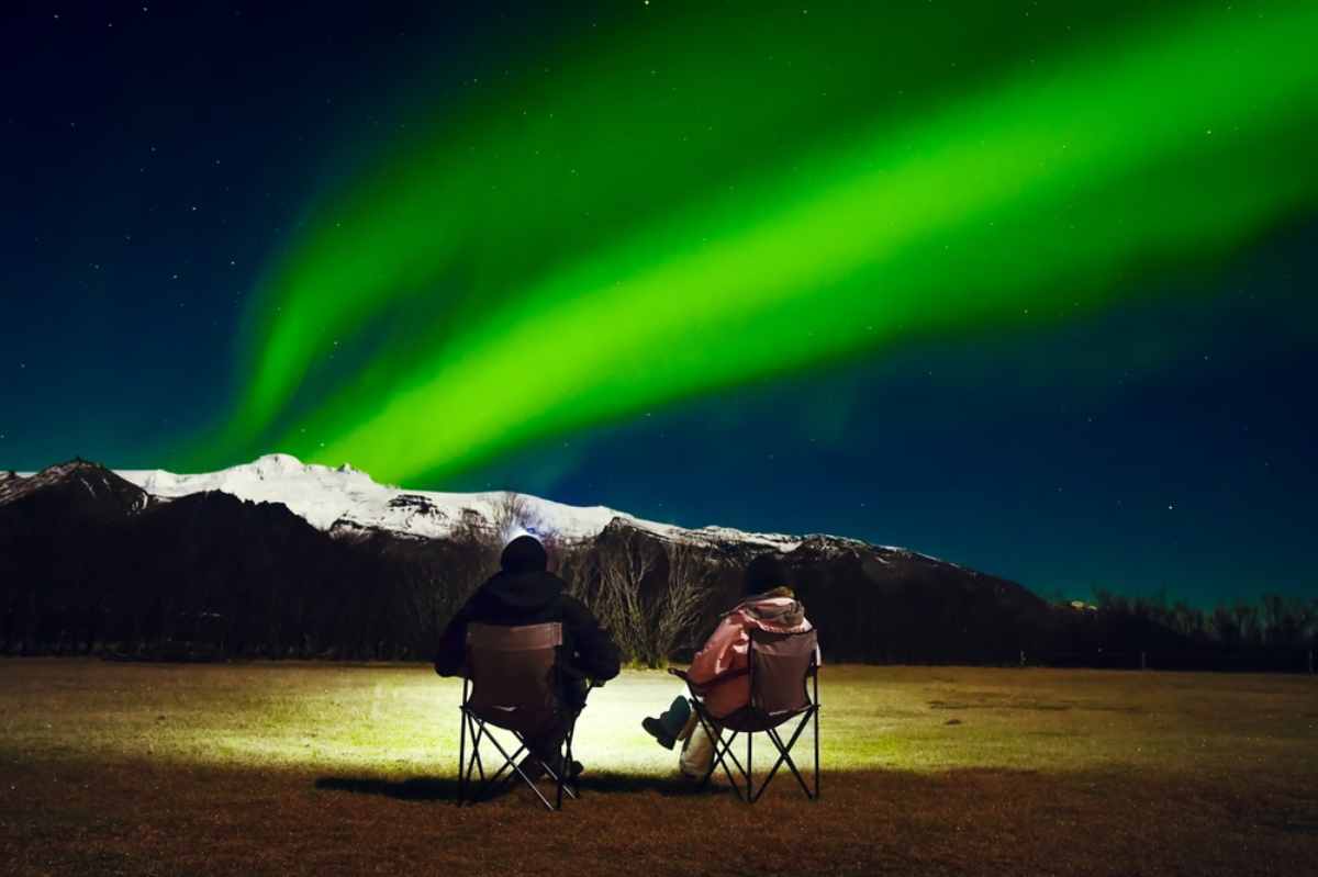 Two people sitting on chairs watching the northern lights in Iceland.