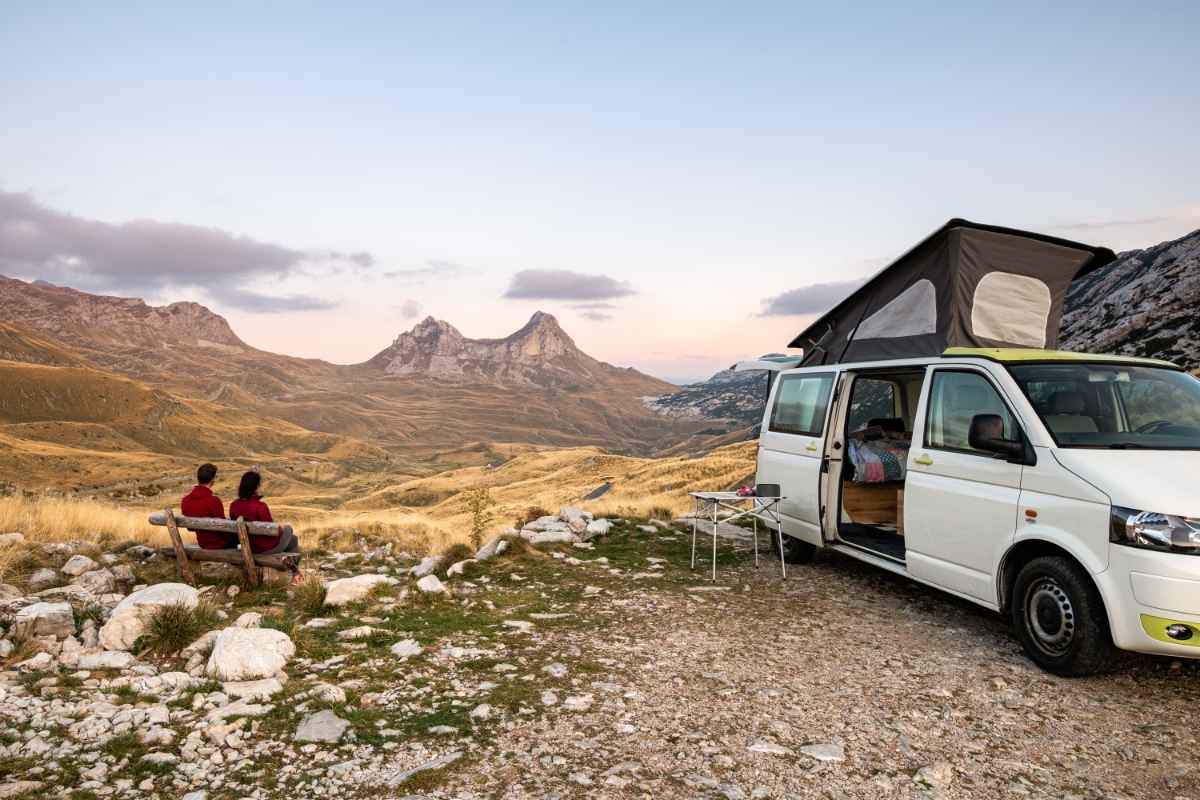 Tourists seating on a bench by a california campervan in a scenic landscape