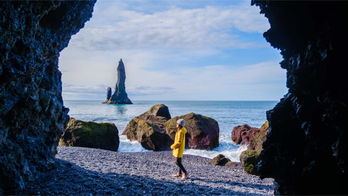 Tourist in a yellow raincoat standing by a cave in reynisfjara black beach