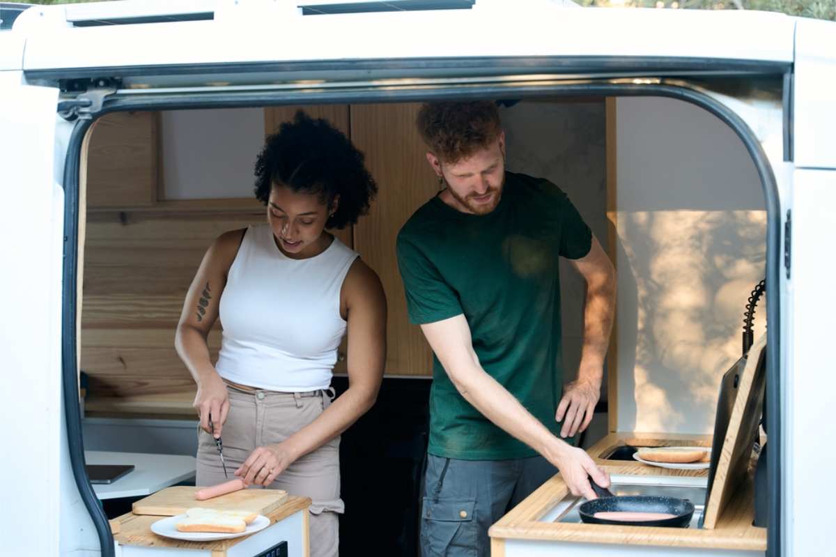 Couple cooking sausages inside of a motorhome 
