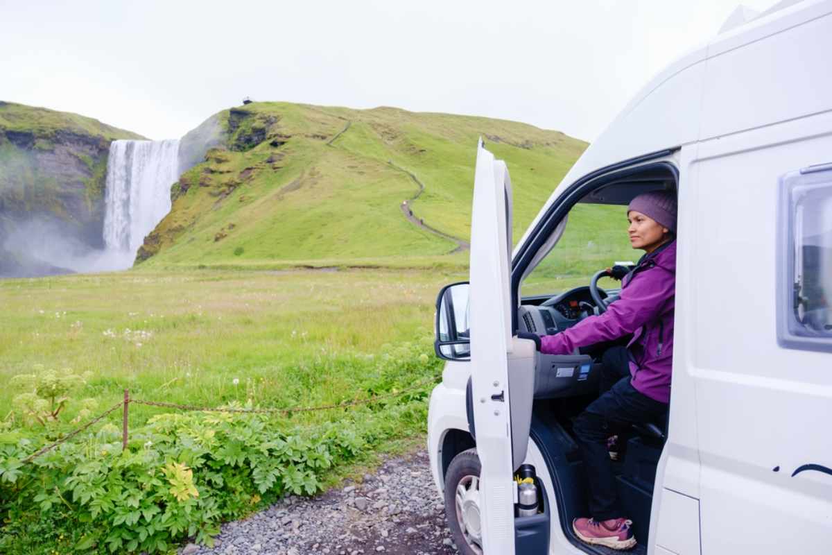 Traveler holding a campervan door near Skógafoss waterfall in Iceland on a windy day