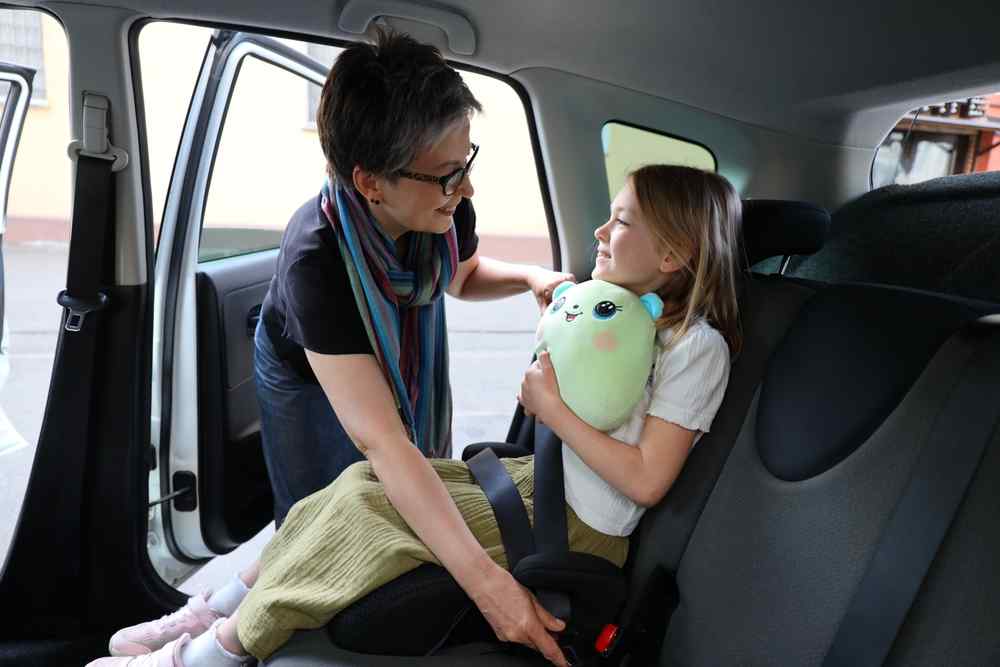 Approval for car seat in Iceland Adult helping a child fasten a car seat inside a vehicle.